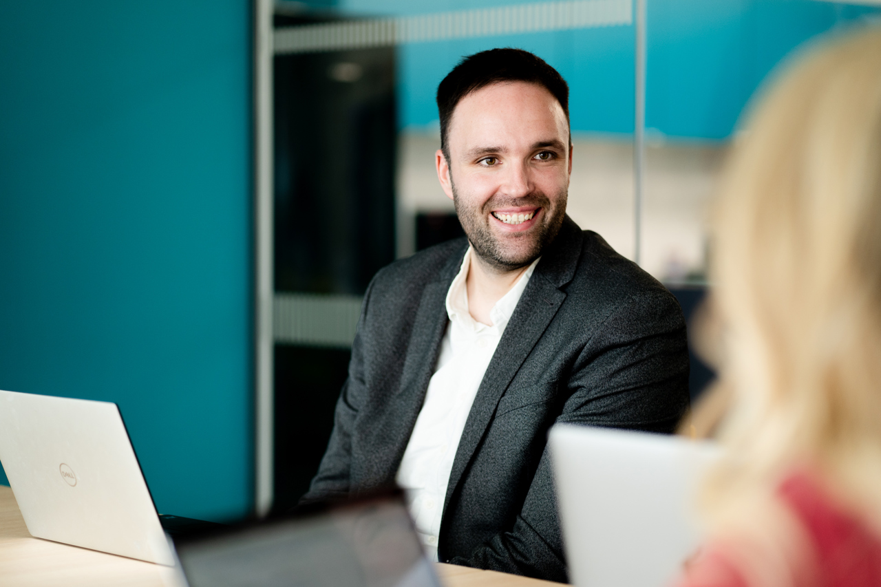 Smiling man sat in an office meeting room with laptop open