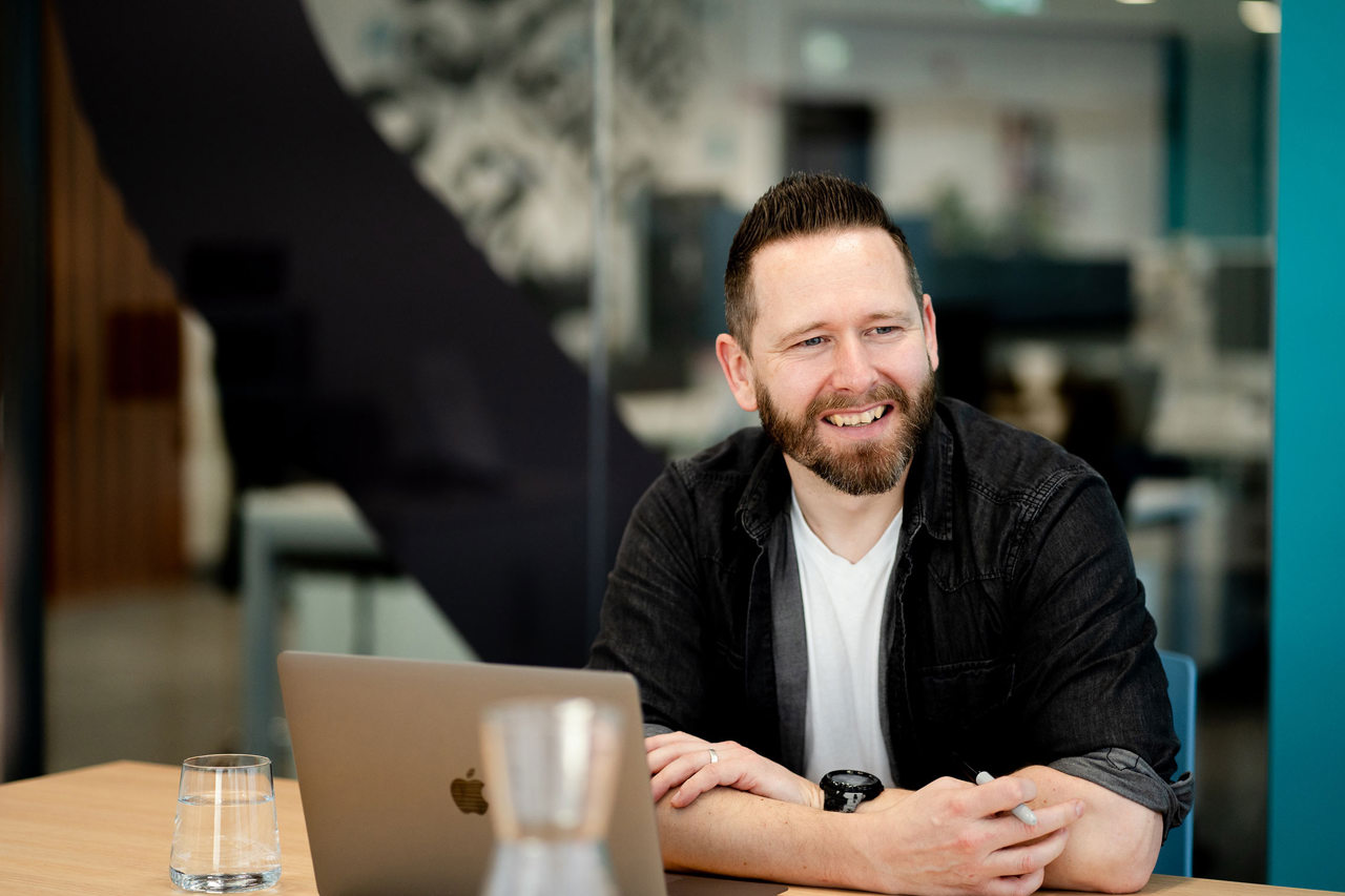 A man at a desk in an office meeting room smiling